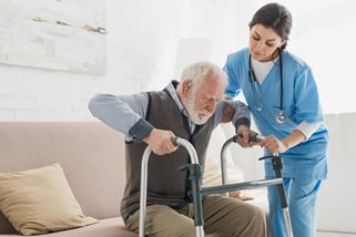 Healthcare provider helping a man stand using a walker. 