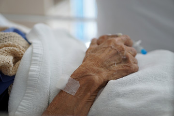 Elderly man in a hospital bed, with arms folded over abdomen. 