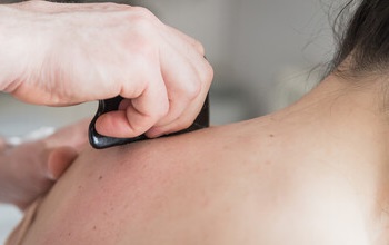 Using a gua sha jade scraper on a client's shoulder.