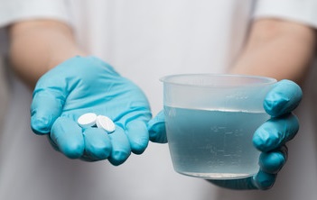 Nurse holding 2 white pill medications and glass of water 