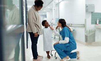 A nurse bending a knee to speak to a small child patient pushing an IV pole