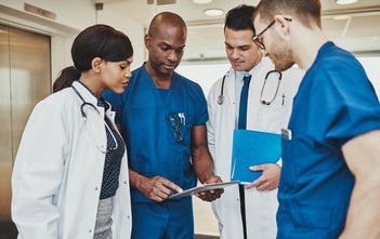 Team of four doctors and nurses in a huddle, discussing patient records
