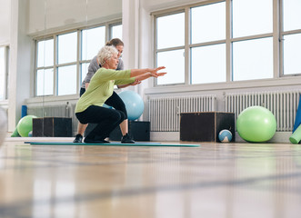 Woman squating with arms outstretched, assisted by physical therapist. 