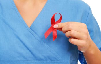 Nurse in blue scrubs holding a red AIDS ribbon to her chest.