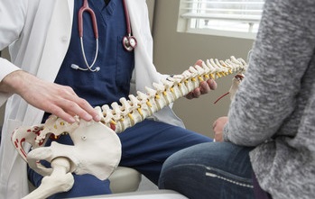 healthcare provider holding a skeleton across his lap demonstrating the vertebral issue to the patient.
