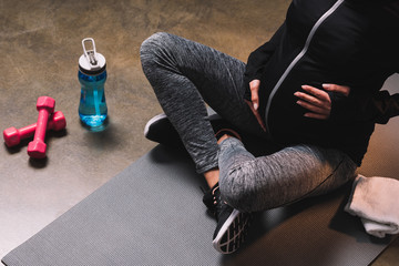 Pregnant woman on yoga mat with light dumbbells.