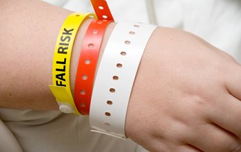 Hospital patients wrist with multiple wrist bands. One says fall risk. 