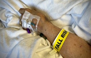 Patient lying in a hospital bed, with a FALL RISK arm band on. 