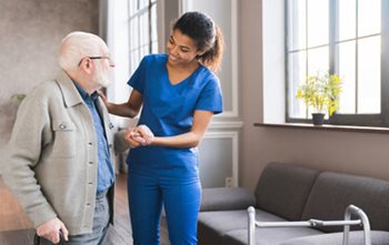 Young woman in blue scrubs assisting an elderly man to walk.