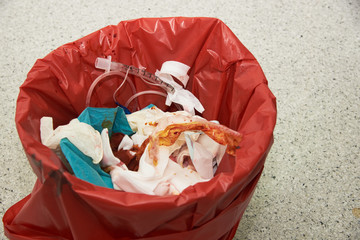 Trashcan lined with a red biohazard bag and contains blood bandages. 