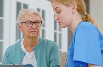 Nurse aid discussing with angry looking elderly female patient